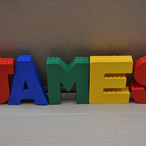 Hand painted papier mache lego letters spelling JAMES in red, blue, green & yellow