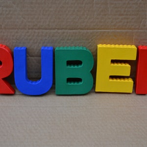 Hand painted papier mache lego letters spelling RUBEN in red, blue, green & yellow
