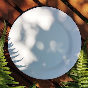 May include: A white ceramic plate with a black rim sits on a wooden surface. The plate is empty and has shadows from the sunlight.