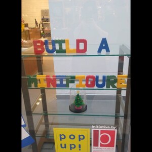 Hand painted papier mache lego letters sign in red, blue, green & yellow in a shop window