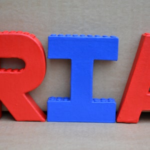 Hand painted papier mache lego letters spelling RIA in red & blue