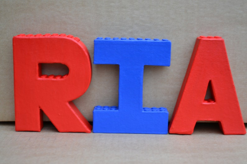 Hand painted papier mache lego letters spelling RIA in red & blue