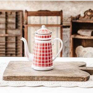 Könnte beinhalten: Rote und weiße karierte Emaille-Kanne mit weißem Deckel und silbernem Griff. Die Kanne steht auf einem Holzbrett.