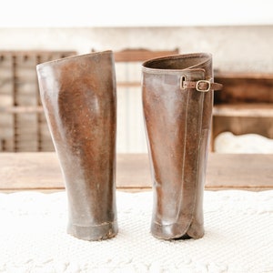 May include: A pair of brown leather riding boots with a buckle strap on one boot.