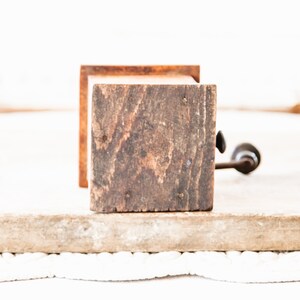 May include: A vintage wooden coffee grinder with a dark, weathered appearance. The grinder features a square wooden body with visible wood grain and a metal handle. The design suggests a rustic, antique aesthetic.