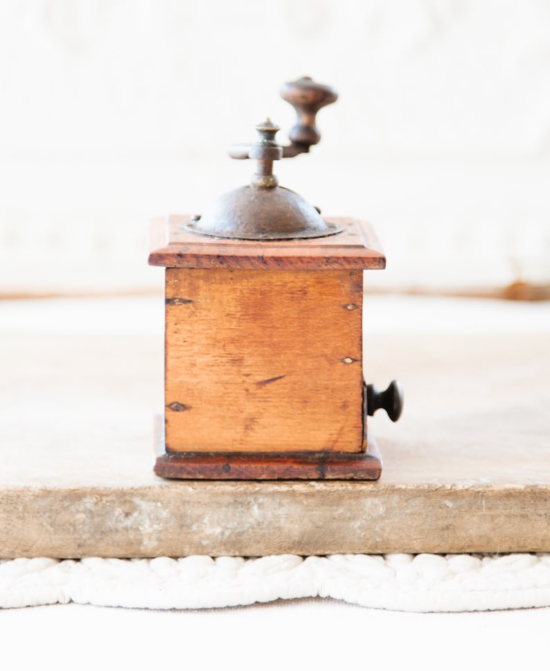 May include: A vintage wooden coffee grinder with a metal top and crank. The wooden box is a warm brown color, and the metal components show signs of age. The grinder is a classic kitchen tool.