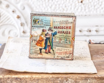 May include: Vintage tin box with a colorful illustration of two children and the text "EENIG ECHTEN HAAGSCHE HOPJES oudtijds geheeten BOPBONS VAN BARON".