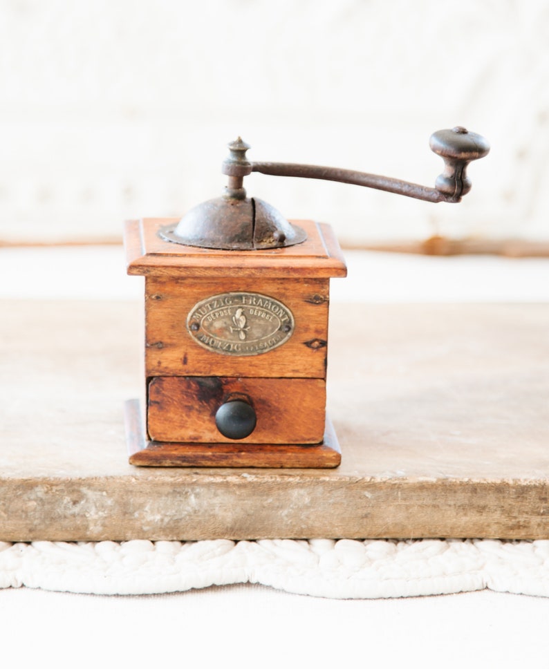 May include: A vintage wooden coffee grinder with a metal crank and a small drawer. The grinder has a dark brown finish and a metal plate with text. The handle is dark brown and the drawer has a black knob.