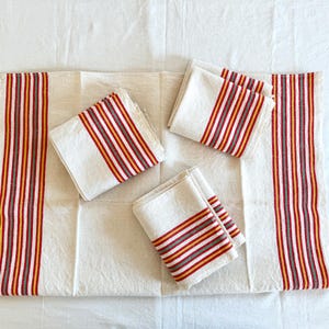 May include: Set of five white linen tea towels with red, orange, and gray stripes. The towels are folded and arranged on a white surface.