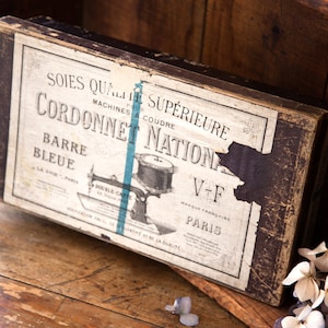 May include: Vintage box for sewing machine thread, labeled "Soies Qualite Superieure" and "Cordonnet Nation Barre Bleue." The box is brown with a blue and white label and features a drawing of a sewing machine.