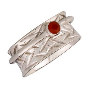 May include: A silver-colored spinner ring with a textured band and a small, round, red gemstone. The ring has a central band that spins freely, and the band has a repeating pattern of diagonal lines.