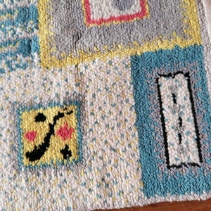 May include: A colorful rug with a geometric pattern. The rug is made of woven fabric and has a fringe border. The rug features a variety of colors, including blue, yellow, white, and pink.