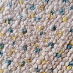 May include: Close-up of a beige carpet with a textured surface. The carpet has a repeating pattern of small blue and yellow dots.