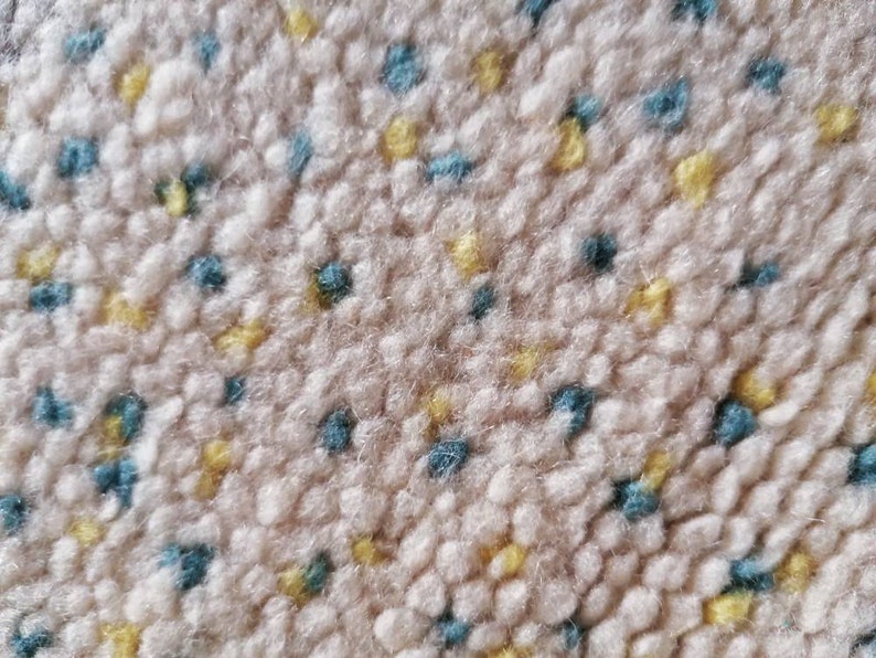 May include: Close-up of a beige carpet with a textured surface. The carpet has a repeating pattern of small blue and yellow dots.