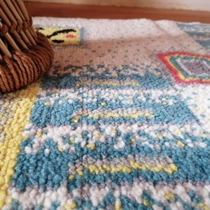 May include: A close-up of a colorful rug with a woven pattern in shades of blue, yellow, white, and red. The rug has a textured surface and is made of soft fibers.