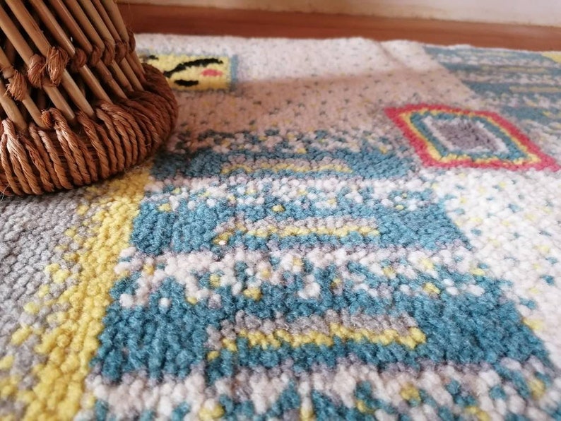 May include: A close-up of a colorful rug with a woven pattern in shades of blue, yellow, white, and red. The rug has a textured surface and is made of soft fibers.