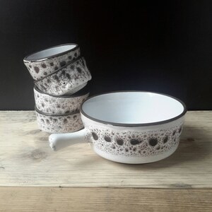 Puede incluir: Un juego de cuatro cuencos de cerámica blanca con un patrón moteado marrón. Los cuencos están apilados uno encima del otro, con el cuenco más grande en la parte inferior. Los cuencos tienen un interior blanco y un borde marrón.