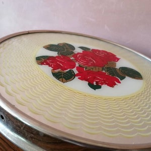 May include: Oval-shaped, vintage vanity tray with a silver-toned metal frame. The tray features a central design of red roses with green leaves on a white background. The outer edge has a scalloped, cream-colored pattern.