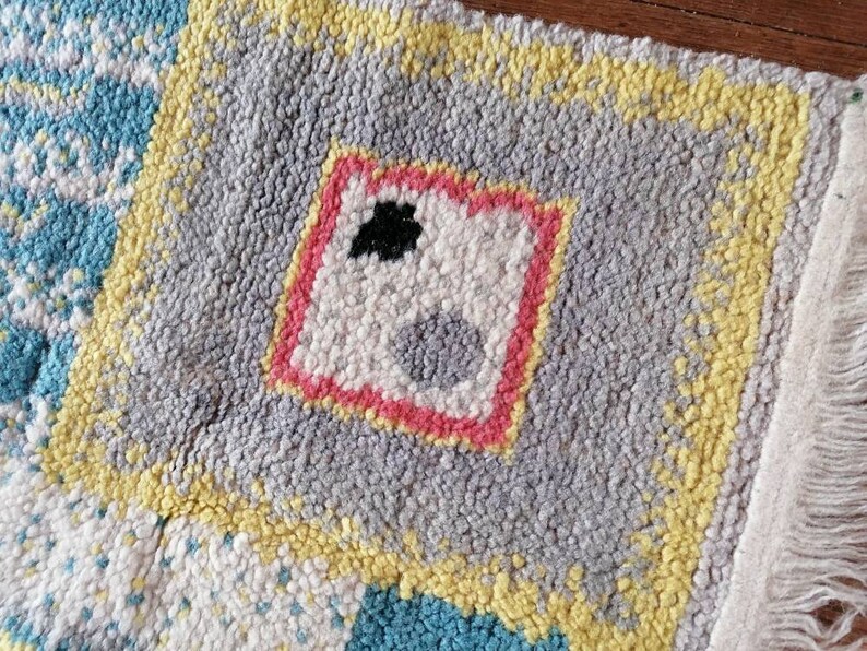 May include: A colorful rug with a geometric design. The rug is made of a soft, fuzzy material and has a fringe border. The rug features a central square with a pink border and a white interior with a black and gray design.