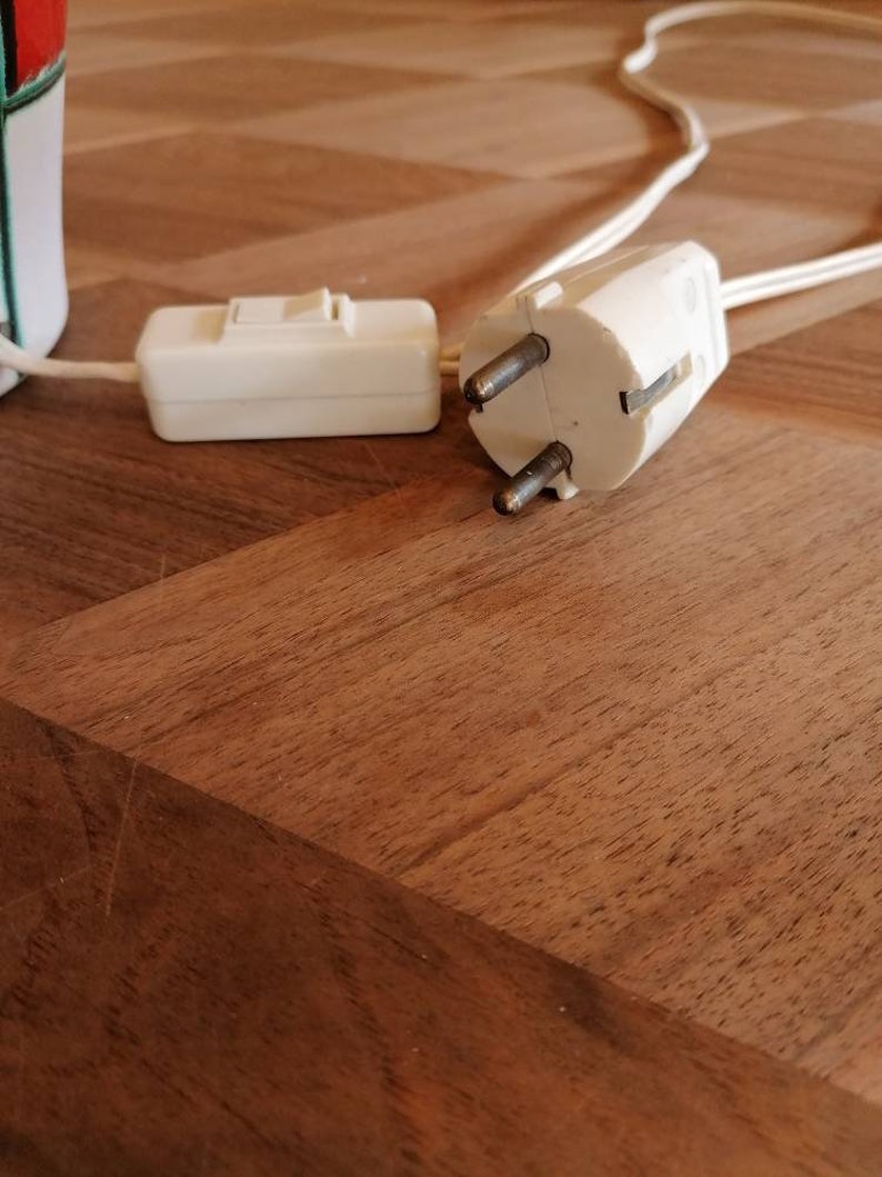 May include: A white electrical plug with two prongs and a ground pin, connected to a white cord. A white inline switch is also visible. The items are on a wooden surface. Electrical components.