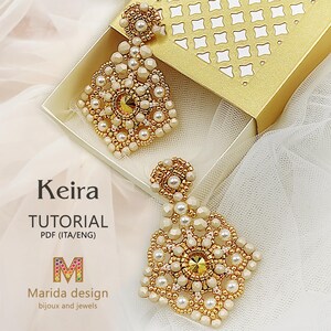 Puede incluir: Un par de pendientes de cuentas doradas y crema con un gran cristal en el centro. Los pendientes están en una pequeña caja con un patrón dorado y blanco. El texto "Keira TUTORIAL PDF (ITA/ENG) Marida design bijoux and jewels" está debajo de los pendientes.
