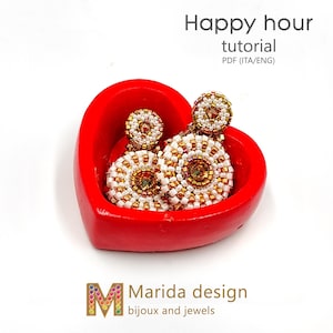 May include: A pair of white and gold beaded earrings with a round shape, displayed in a red heart-shaped dish. The earrings are made with small beads and have a delicate, feminine design. The text "Happy hour tutorial PDF (ITA/ENG)" is visible above the earrings. The text "Marida design bijoux and jewels" is visible below the earrings.