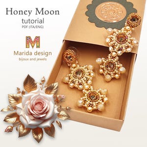 Può includere: Un paio di orecchini dorati con perline a forma di stella, in una scatola marrone con una rosa e foglie sul lato sinistro. La scatola ha un'etichetta che recita "Honey Moon tutorial PDF (ITA/ENG) M Marida design bijoux and jewels".