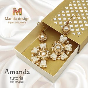Può includere: Orecchini color oro con perline bianche e dorate, con una perla centrale e un design a forma di croce. Gli orecchini sono esposti in una scatola dorata. L'immagine include il testo "Marida design bijoux and jewels" e "Amanda tutorial PDF (ITA/ENG)".