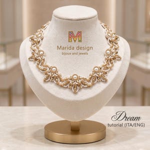 May include: A beaded necklace featuring white and gold beads arranged in a floral pattern on a beige display bust. The text Marida design bijoux and jewels and Dream tutorial (ITA/ENG) is visible on the display and near the base.