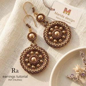 May include: A pair of bronze-toned beaded earrings featuring a circular design with a central bead surrounded by smaller beads. A tag reads Marida design bijoux and jewels, and text on the page reads Ra earrings tutorial PDF (ITA/ENG).