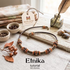 Peut inclure: Un collier en cordon de cuir marron orné de perles complexes dans des tons cuivre, bronze et vert foncé. Le collier comprend des perles sphériques métalliques et de petites perles de rocaille disposées en motif. Une étiquette porte le texte Marida design.
