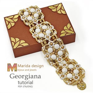 Può includere: Un bracciale largo di perline con un motivo ripetuto di perline bianche rotonde e perline dorate sfaccettate. Il testo Marida design bijoux and jewels Georgiana tutorial PDF (ITA/ENG) è stampato nell'angolo in basso a sinistra dell'immagine.