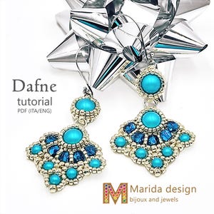 Può includere: Un paio di orecchini di perline turchesi e blu con finitura in metallo argentato. Gli orecchini hanno un design geometrico con una grande pietra turchese al centro e perline turchesi e blu più piccole sui bordi. Il testo "Dafne tutorial" è visibile.