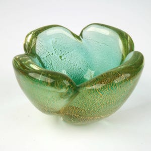 以下が含まれることがあります： ユニークな花の形をした手作りのガラスボウル。緑と金の色の混合で、内側は明るいターコイズ色でテクスチャ加工されています。ガラスは光沢のある仕上がりで、装飾的な魅力を高めています。