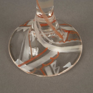 May include: Clear glass goblet with a white and orange swirl design on the base.