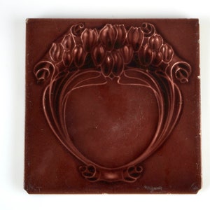 May include: A square, brown ceramic tile with a raised design of stylized tulips and leaves. The tile has a glossy finish.