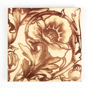 May include: A vintage ceramic tile with a brown floral design. The tile features a large poppy flower with intricate details and surrounding foliage.