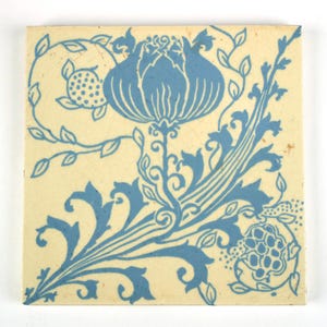 May include: A square ceramic tile with a cream-colored background and a blue printed design featuring a central large flower surrounded by scrolling vines, leaves, and smaller circular fruit-like elements with a visible crackle glaze finish.