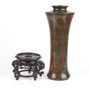 May include: A dark brown wooden stand with intricate carvings and a bronze vase with a mottled green and red patina.