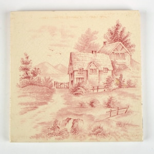 May include: A square ceramic tile featuring a monochromatic reddish-brown transfer print of a rural landscape. The scene depicts two cottages nestled among trees, a winding path, a wooden fence, and distant rolling hills under a soft sky.