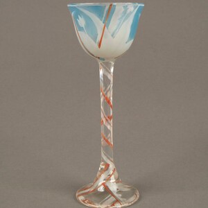 May include: A tall, clear glass goblet with a wide, flared bowl. The bowl is decorated with a blue and white swirl pattern, and the stem is decorated with a red and white swirl pattern.