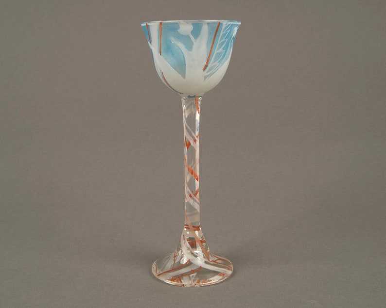 May include: A clear glass goblet with a white and blue design on the bowl and a spiral pattern of white and orange on the stem. The goblet has a wide base.