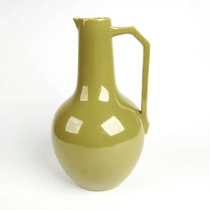May include: A glossy, olive-green ceramic pitcher with a rounded body and a tall, slender neck. It features a distinctive angular handle and a pouring spout. The pitcher is a decorative item, suitable for displaying flowers or as a standalone art piece.