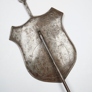 Puede incluir: Un signo del zod&iacute;aco de metal para Tauro, con un dise&ntilde;o de toro y la palabra "Tauro" inscrita en el escudo. El signo est&aacute; unido a una larga varilla de metal.