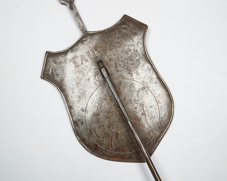Puede incluir: Un signo del zod&iacute;aco de metal para Tauro, con un dise&ntilde;o de toro y la palabra "Tauro" inscrita en el escudo. El signo est&aacute; unido a una larga varilla de metal.