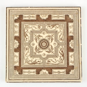 May include: A square tile with a brown and white geometric pattern. The pattern features a central square with a floral design and four stylized dolphins in each corner. The tile is surrounded by a border of brown and white lines.