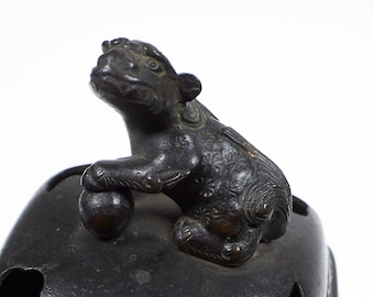 May include: A black bronze incense burner with a detailed lion finial. The lion is sitting on a ball and has a detailed face and body.