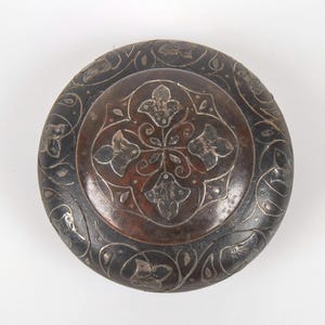 May include: A round, dark brown wooden box with intricate silver floral designs inlaid into the surface.