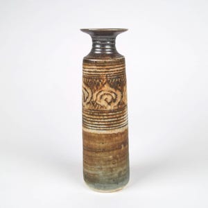May include: A tall, brown and white ceramic vase with a geometric design. The vase has a wide, flat top and a narrow base.