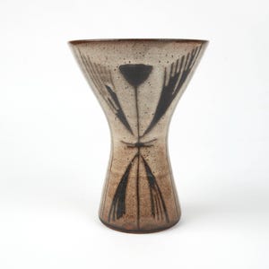 Könnte beinhalten: Eine Keramikvase mit gesprenkelter beige-brauner Oberfläche. Die Vase hat eine ausgestellte Oberseite und eine schmale Taille mit schwarzen abstrakten floralen Designs. Die Vase ist etwa 25 cm hoch.